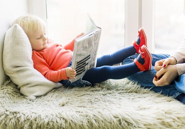 toddler girl reading with her feet propped up on mom